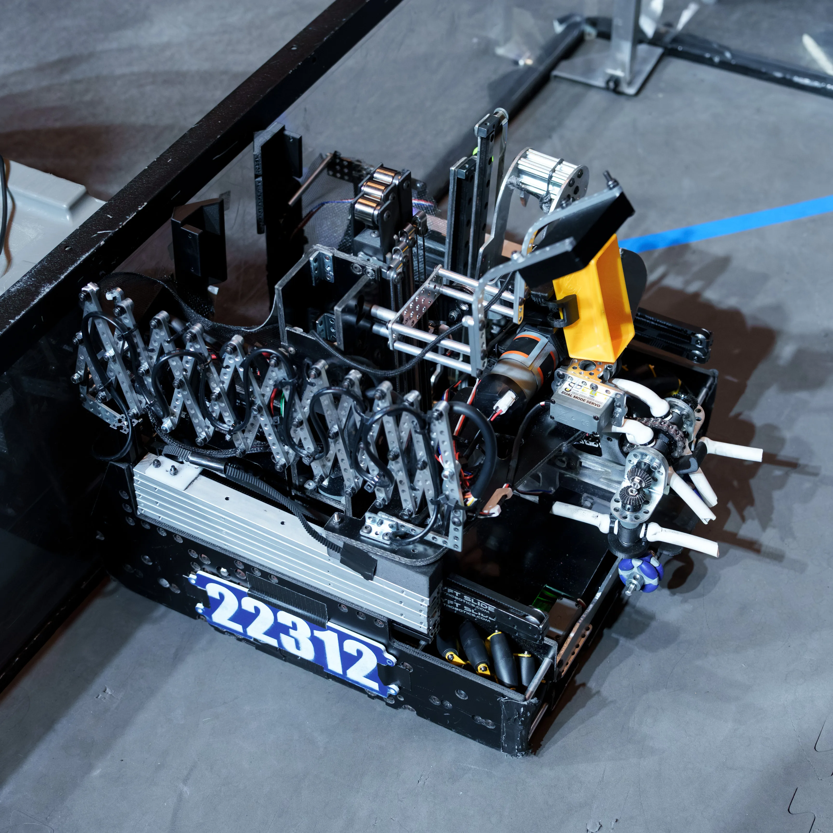 Team 22312’s FTC robot photographed from above on a competition field: a black chassis numbered 22312, with a scissor-linkage extension, a linear slide, and a yellow intake claw at the front.